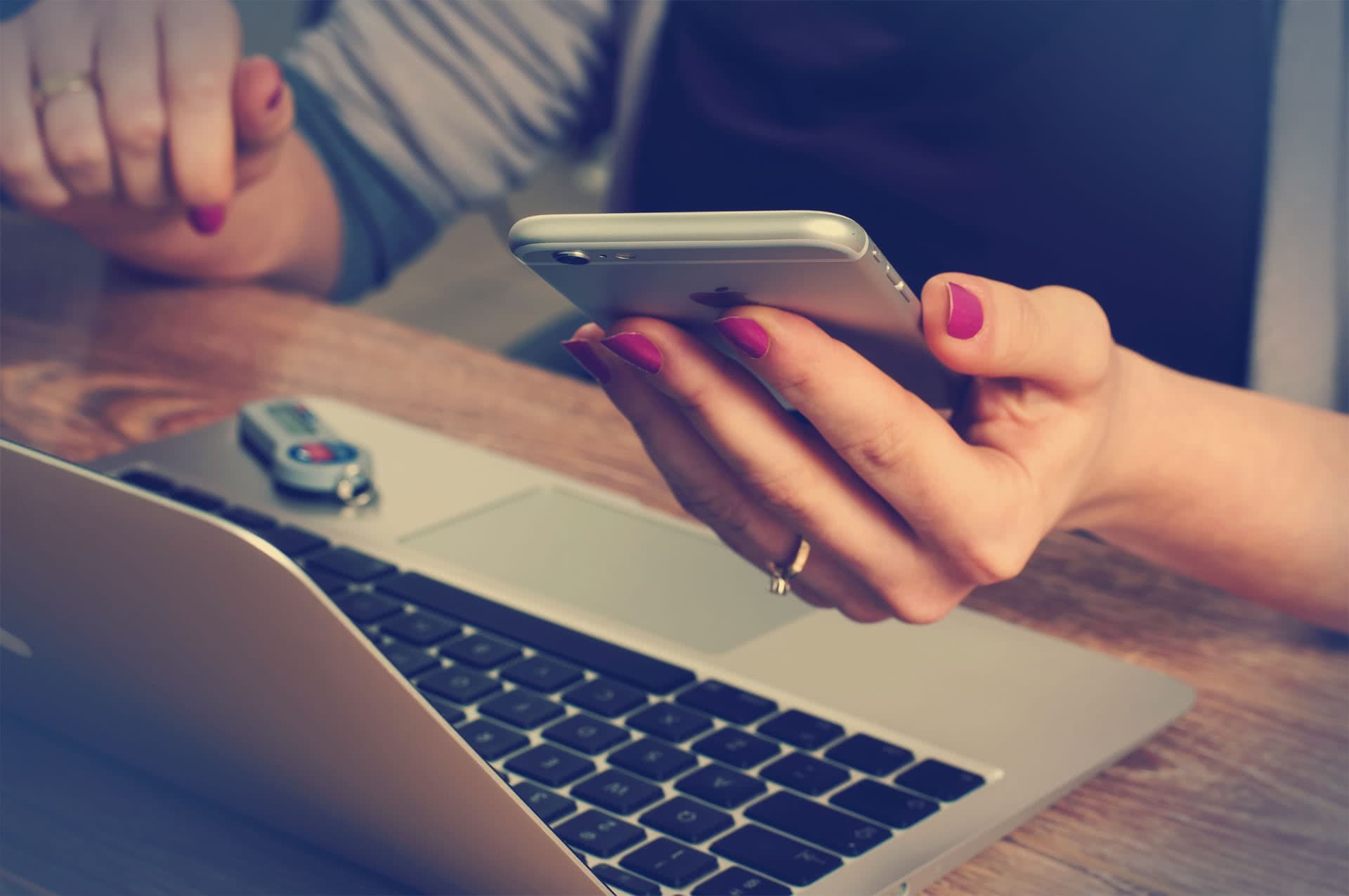 Eine Hand hält ein Smartphone vor einem aufgeklappten Laptop
